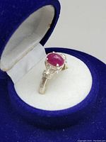 Close-up of the ring inside a blue velvet box showing the red ruby stone and silver band.