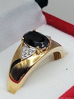 Close-up angled view of the ring showing the black onyx center stone and side white stone accents set in gold-tone sterling silver.