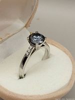 Close-up side angle of the sterling silver ring with grey moissanite center stone in a cream velvet ring box.