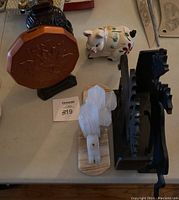 Overview of the lot showing the penny bank, owl bank, piggy bank, marble cactus bookends, and cast iron moose bookends placed on a table.