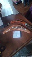 Two hand painted wooden boomerangs displayed on a wooden table with MaxSold lot number 277 visible.