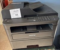 Front view of Brother MFC-L2730DW printer showing paper output slot and control panel.