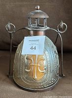 Front view of the glass and metal candle lantern showing embossed fleur-de-lis on the glass and metal frame with vented top dome.