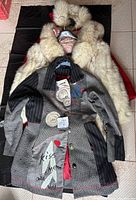 Photo showing three coats stacked: a cream fur coat, a patchwork multicolored coat, and a red coat underneath