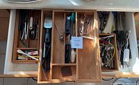 Opened drawer with assorted culinary utensils including forks, various cooking tools, peelers, and scissors.