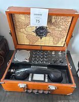 Open wooden case with Spirit of St. Louis field phone showing handset, control knobs, connector ports, speaker, and world map inside lid.