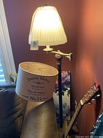 Photo of floor lamp illuminated, showing beige Paris Metro shade and harp structure.