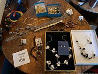Wide view of all jewelry items on wooden table showing various necklaces, bracelets, brooches, and earrings