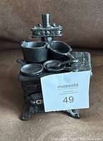 Front view of the miniature cast iron stove with some accessories placed on top showing details.