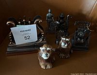 Steel pencil sharpeners resembling vintage objects and two small lion figurines arranged on a brown surface.