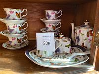 Full view of the Royal Elfleda butterfly patterned tea set including teapot, sugar bowl with spoon, creamer, plate with pie server, and stacked teacups with saucers.