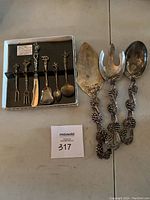 Pie/cake server, large salad fork and spoon with ornate pinecone and branch design handles, alongside a box of six small appetizer forks with decorative handles.