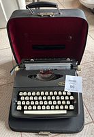 Full view of the Singer Model T-63 manual typewriter seated inside its open original black carrying case with red interior lining on tiled floor.