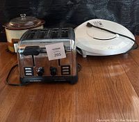 Wide shot of lot showing crock pot, toaster, and grill on wooden surface.