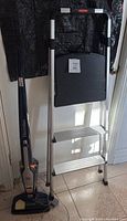 Electrolux Ergorapido lithium cordless stick vacuum next to Rubbermaid 3-step ladder, shown full height with vacuum on floor and ladder upright.
