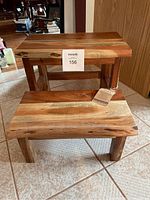 Two wooden step stools placed on tiled floor near wooden door. Variations in wood grain and color visible on both stools.