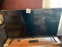 Full view of the LG television on wooden surface showing the screen, legs, and remote control placed in front.