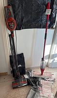 Full view of Shark Rocket upright vacuum cleaner with cord, base, and multiple accessories on floor beside it, along with the red Vileda Promise Max microfibre spray mop.
