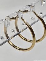 Pair of gold hoops displayed on acrylic stand, side view