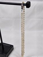 Full view of the pearl necklace hanging on a stand showing graduated size pearls, clasp visible at top