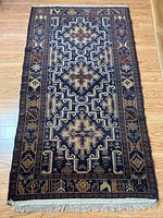 Full view of the blue area rug laid flat on a wooden floor showing the entire rug including its fringe and geometric pattern.