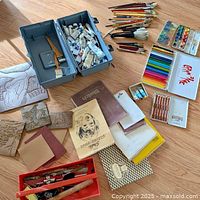 Overview of contents showing large plastic toolbox with paint tubes and brushes, various sketchbooks, colored pencils, watercolor paints, and stencils.