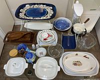 Photo showing entire assortment of Corning Ware, Corelle white platters with decorative motifs, blue bowls, wooden platters, salt and pepper shakers, Brita water pitcher and Worcester Ware metal tray with daisy design.