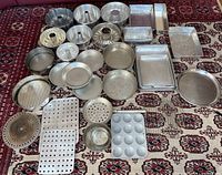 Overhead view of assorted baking ware on patterned rug, showing all types and shapes of pans and trays included in lot.
