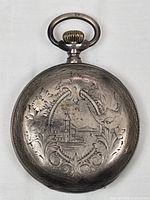 Front side of the hunter pocket watch case showing elaborate engraving including buildings, floral and ornamental details.