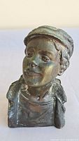 Front view of bronze bust showing the boy's facial features and cap.