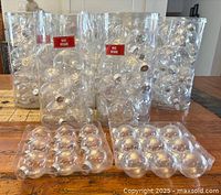 Nine packages of clear flat round plastic ornaments and two packages of plastic ball ornaments arranged on a wooden surface.