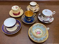 Top view showing all six demitasse cups and saucers arranged on a wooden surface, displaying various colors and gold accents