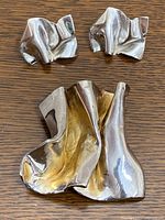 Photo showing pair of silver earrings and a brooch with abstract folded design on wooden surface.