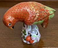 Front profile view of red and green parrot perched on white floral base