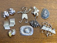 Photo showing all jewelry pieces on a wooden surface including clip earrings, flat rectangular earrings, floral brooches, a textured Boggio labeled brooch, and the 'LOVE' figurative brooch.