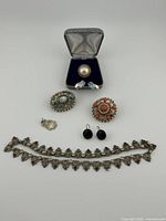 Full lot displayed on white background including ring in box, two brooches, pair of earrings, choker, and removed hand pendant