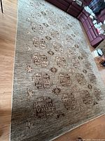 Full view of large rectangular beige and brown Pakistani wool rug on hardwood floor with nearby furniture.