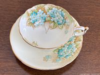 Top-down view of the teacup resting inside the matching saucer, showing the floral hydrangea pattern with mint green and blue flowers and gold trims.