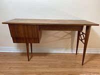 Front view of desk showing overall shape, teak finish, tambour door cabinet and lattice leg support