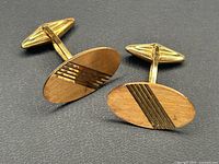 Pair of oval cufflinks on grey background, angled front view showing brushed finish and stripe accents