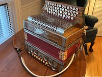 Three-quarter front view of accordion on table showing bellows, grille and strap