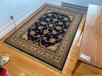 Full view of the rectangular area rug with intricate floral and scroll design, black center field, and multiple bordered edges with fringe.