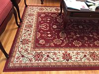 Partial view of rug under coffee table showing red central field and cream border with floral motif