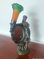Front view of the desk lamp showing the colored glass flower-shaped shade, female figurine, and cherub by the oval mirror.