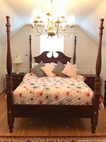 Front view of queen size four-poster bed frame showing carved headboard, turned posts, floral bedding and nightstands on each side.
