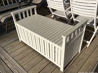 Front angled view of white wooden slatted outdoor bench with storage and armrests on each side, showing construction and condition in daylight.
