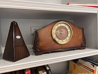 Photo of the Paquet wooden metronome and Seth Thomas mantel clock side by side on a white shelf.