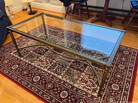 Angled view of rectangular coffee table showing metal frame and clear glass top on patterned rug
