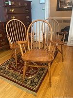 Three oak dining chairs arranged on hardwood floor with a rug beneath some chairs, showing front and side views.