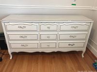 Front view of white dresser with nine drawers, showing metal handles and round knobs on drawers.